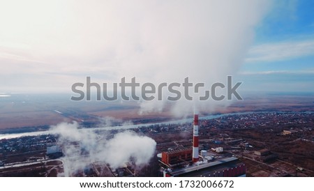 Aerial shot Pipes with smoke: industrial production, plant, air pollution. Dense thick smoke comes from industrial red-white pipes: from a bird's eye view. Industrial zone: smoke comes from the pipe