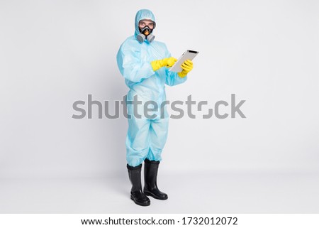 Full size photo of smart doctor man use tablet search read social media ncov epidemic information wear white suit hazmat latex gloves boots breathing mask isolated gray color background