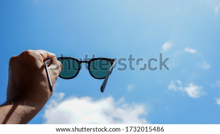 Close up of hands holding sunglasses and sky blue Royalty-Free Stock Photo #1732015486