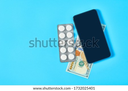 Smartphone near pills and banknote of one hundred dollars on blue background. E-health, e-medicine, payment for services concept. Online purchasing, consultation, medical assistance