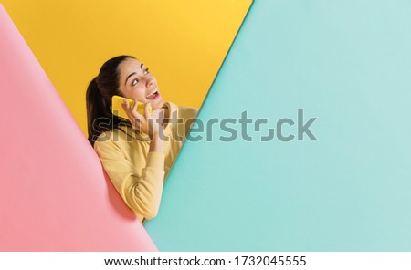 Happy woman with a smartphone. Colorful creative yellow studio background.