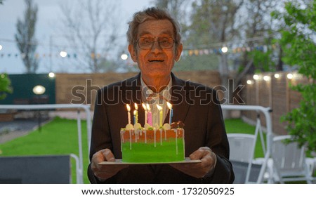 An aged man holds a cake with burning candles.