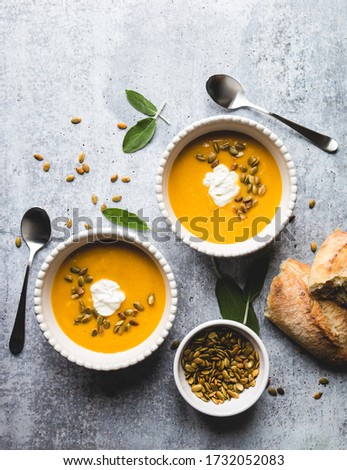 Top view of bowls of butternut squash soup on grey background.