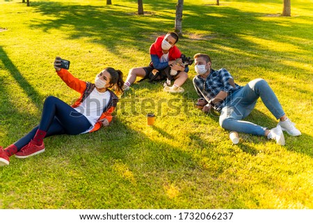 Cheerful university student taking selfie with friends sitting on grass