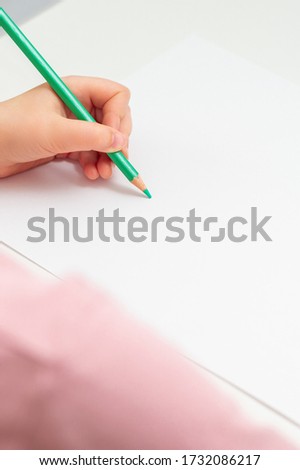 Vertical image of the child's left hand preparing to draw on a white sheet of paper with green pencil. Copy space for text.
