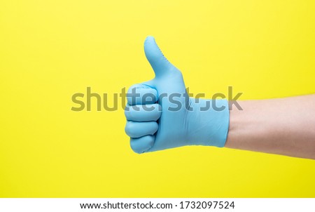 yellow background and hand in medical gloves.male hand in latex medical blue glove shows good luck gesture