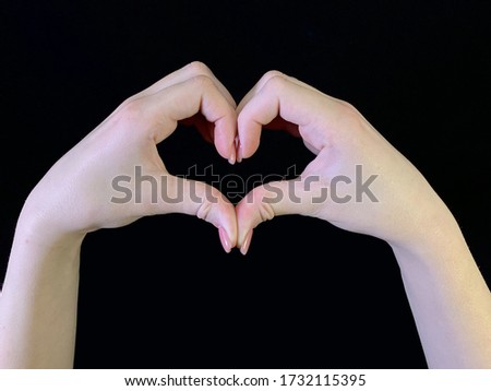 Two hands depict a heart on a black background. Female fingers with a beautiful manicure. Hands of a young girl show a heart sign.