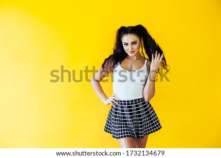 portrait of a beautiful fashionable woman in a T-shirt and skirt on a yellow background