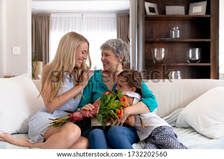 Senior Caucasian woman spending time with her daughter and her granddaughter at home in the sitting room, smiling and interacting.