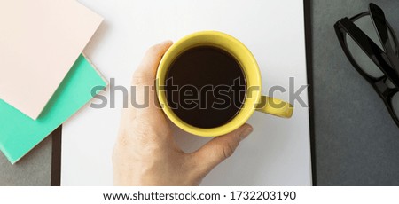 Yellow mug with coffee in hand, desktop, top view.