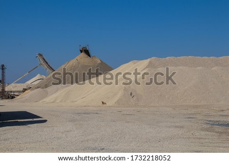 Hills of gravel at a minining plant. Dog at a bottom of the pile. Parts of machinery. Bright blue sky. Puste Ulany, Slovakia