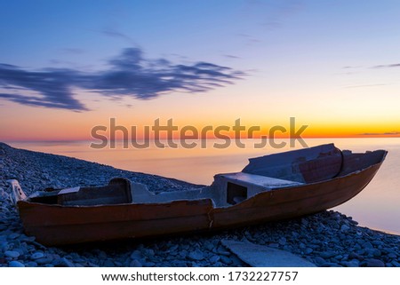 Broken boat laying on a stone beach next to calm ocean with an cloudy sunset as background, at the island of Gotland in Sweden