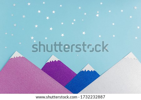 Applique made of colored paper and silver confetti on a blue background. Starry sky and snow-capped peaks of the mountains. Sweet night concept.