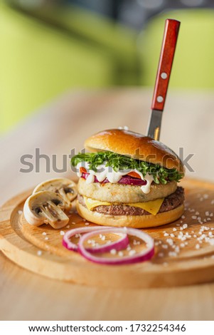 Delicious juicy hamburger on a served wooden board with a stuck knife, on a black background. Cutlets, buns, mushrooms and vegetables. Mushroom hamburger.