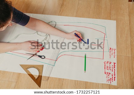 Designer creates a model. Female hands with a manicure do the layout of the sewing pattern on paper
