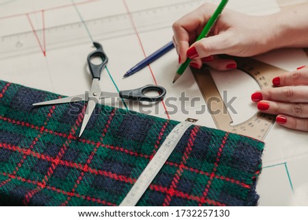 Designer creates a model. Female hands with manicure make markings on a piece of Scottish fabric with a flexible centimeter
