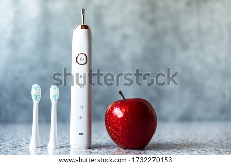 Modern white sonic or electric toothbrush with replacement heads and red apple. Concept of professional oral care and healthy teeth by using sonic smart toothbrush. Minimal design