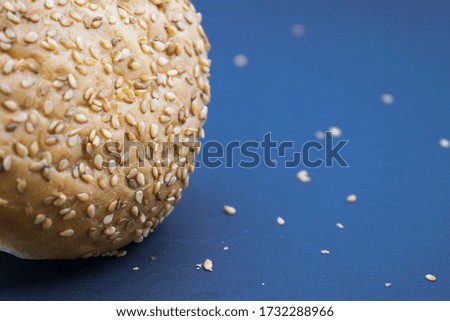 on the left on a blue background a bun sprinkled with sesame seeds