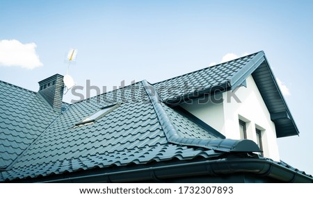 Roof of a new home. Ceramic chimney, metal roof tiles, gutters, roof window. TV antennas attached to the chimney. Single family house. Royalty-Free Stock Photo #1732307893