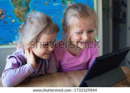 Two beautiful sisters watch cartoons and entertainment on a tablet, games on a laptop, modern children and their development