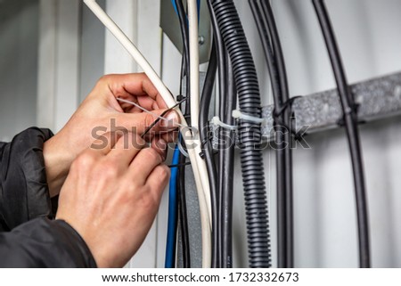 Hands fasten the ties on the cable, which are on the cable tray. Close-up. Horizontal orientation. Royalty-Free Stock Photo #1732332673