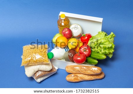 White box with Food supplies crisis food stock for quarantine isolation period on blue.Vegetables, herbs, rice, pasta, canned food, oil, sugar, buckwheat.Quarantine,coronavirus,food delivery,Donation