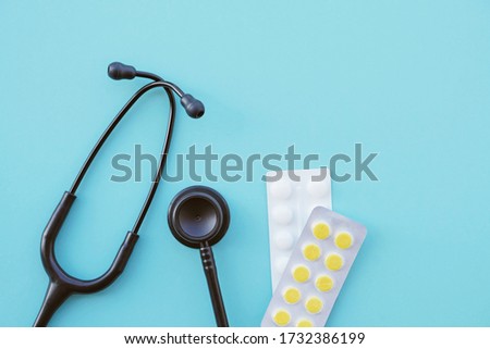 Black modern stethoscope and tablets on light blue background, close up. Medicine and healthcare, cardiology, medical education. Acoustic medical device. Space for text. Flat-lay, top view.