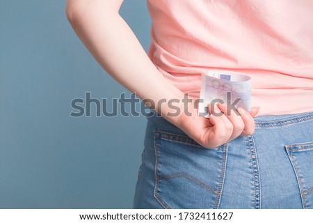 woman hides behind a bill of 500 euros, blue background, copy space, hide money, save for a rainy day, financial problems concept