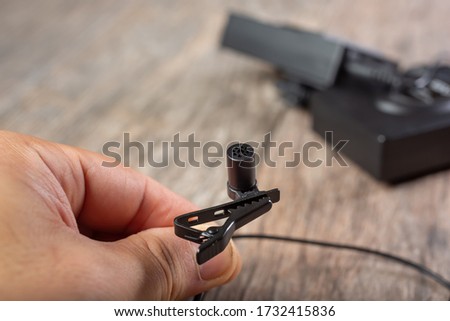 A closeup view of a hand holding a lavalier microphone and lapel clip.
