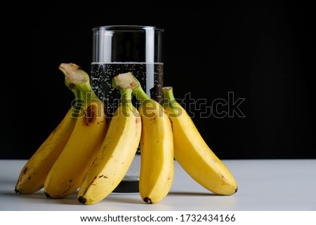 Glass of water and banana fruit on black background.