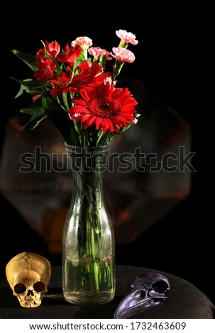Flowers: A vase of flowers, red, pink with green stems, shot in studio with skulls at the base.