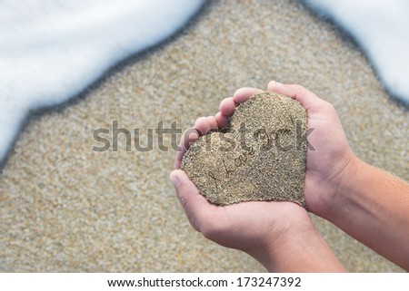 Hands holding a sand in form of the heart with text "I love you" - st.valentines day concept