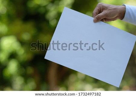 hand holding a white paper on green background