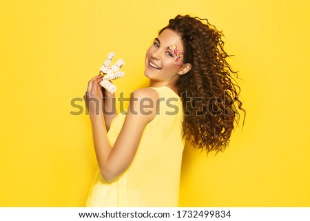 Image of beautiful smiling woman with afro curls isolated over vivid yellow wall background holding cake. Say diets NO in quarantine! Happy with sweets.