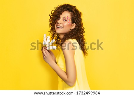 Image of beautiful smiling woman with afro curls isolated over vivid yellow wall background holding cake. Say diets NO in quarantine! Happy with sweets.