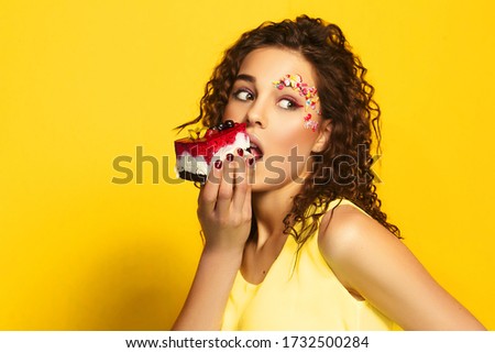 Image of beautiful woman with stylish trendy hairstyle isolated over yellow wall background holding and eating cake. Candy girl with sweet tooth