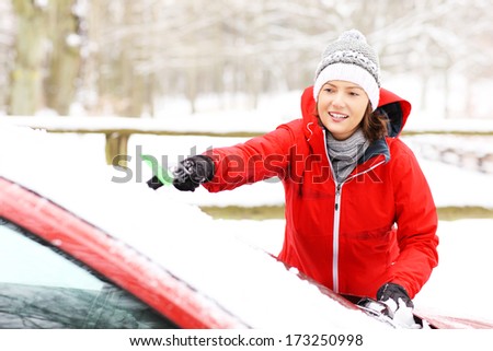 A picture of a young woman cleaning a windshield from the snow