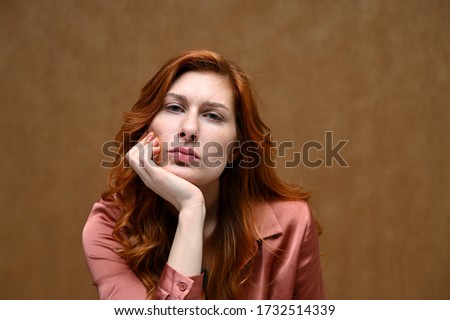 Photo portrait on a beige background of a calm pretty young woman in a pink shirt with long beautiful red hair. Studio shot.