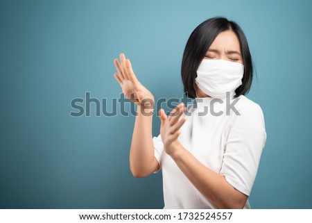 Don't touch me. Asian woman wearing hygiene mask panic and disguted showing hand stop sign and standing isolated over blue background. Health care concepts.
