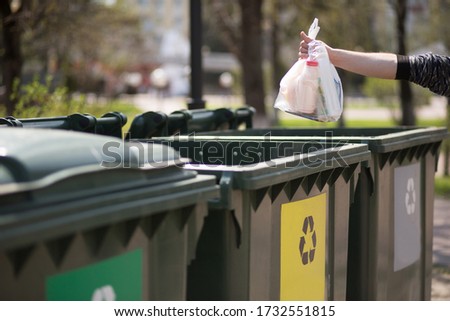 Hand with a bag of plastic garbage over containers for separation and sorting in Russia with the words: Glass, plastic, household waste. Waste sorting, the concept of eco-friendly garbage collection