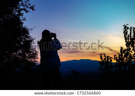 Silhouette of a woman photographing a sunset
