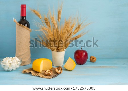 Bottle of wine, cheese and wheat ears for Jewish holiday Shavuot on blue wooden background with copy space.