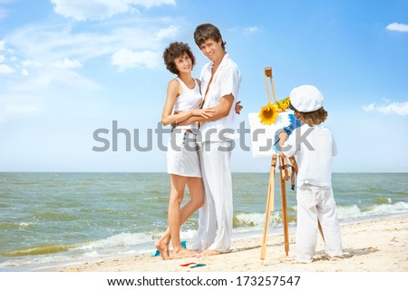 Happy parents pose for child, drawing picture on sea beach