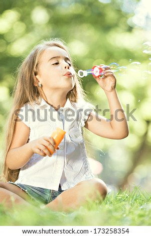 Little happy girl blowing soap bubbles in the parc