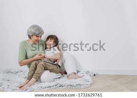 A little boy and his grandmother are having fun together against a light background