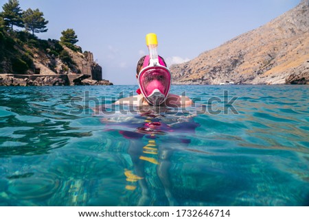 Snorkeler in pink mask, snorkeling man in full face mask, summer vacation activity, swimming in the warm tropical sea, seashore and fishes, starfishes near rocks, Italy