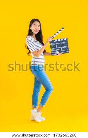 Portrait beautiful young asian woman show clapper movie board on yellow isolated background