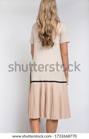 A vertical shot of the back of a blonde female model in an elegant beige dress