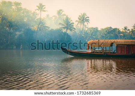 A traditional house boat is anchored on the shores of a fishing lake in the palm tree jungle at sunset, in the Backwaters, a popular destination for yoga retreats and nature lovers in Kerala, India Royalty-Free Stock Photo #1732685369