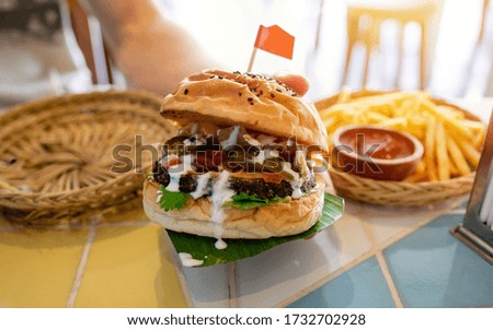 Freshly made of healthy vegan burger,  dish represented on wooden plate. Man's hands taking vegan burger from plate in vegan restaurant or cafe.
